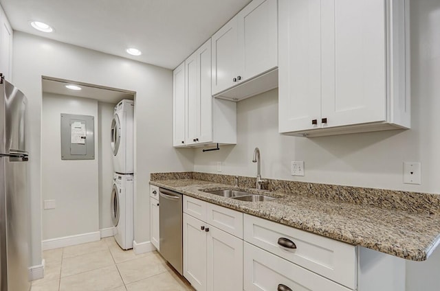 kitchen with sink, white cabinetry, appliances with stainless steel finishes, stacked washing maching and dryer, and light stone countertops