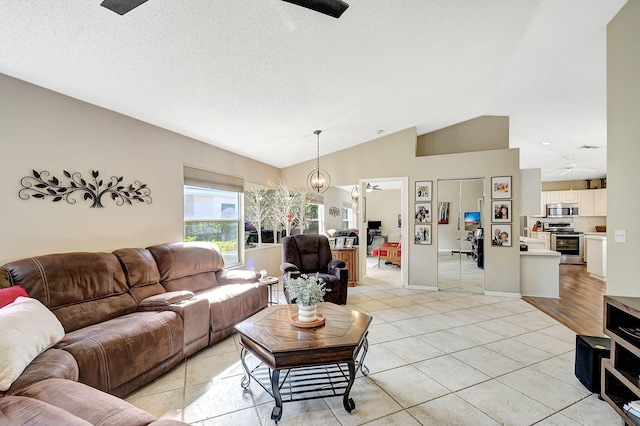 living room featuring lofted ceiling, light tile patterned floors, ceiling fan with notable chandelier, and a textured ceiling