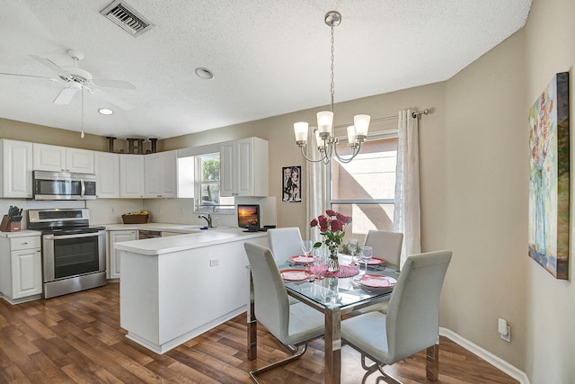 kitchen with appliances with stainless steel finishes, pendant lighting, white cabinets, kitchen peninsula, and dark wood-type flooring