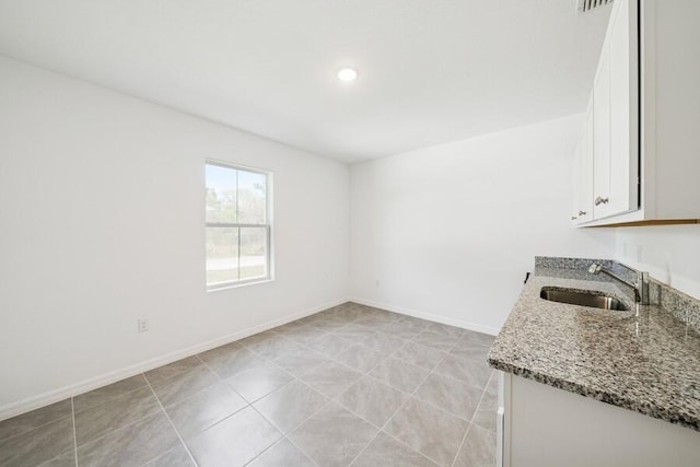 interior space with baseboards, light stone countertops, light tile patterned floors, white cabinetry, and a sink