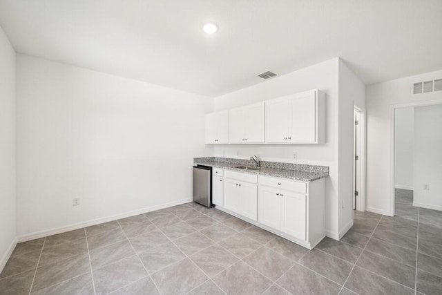 kitchen featuring visible vents, a sink, white cabinetry, light stone countertops, and dishwasher