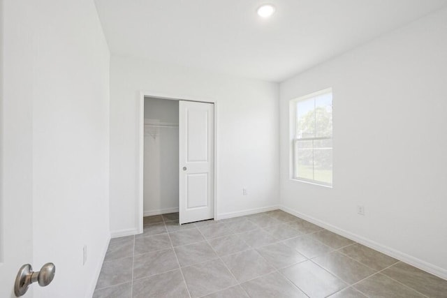 unfurnished bedroom featuring light tile patterned floors, baseboards, and a closet