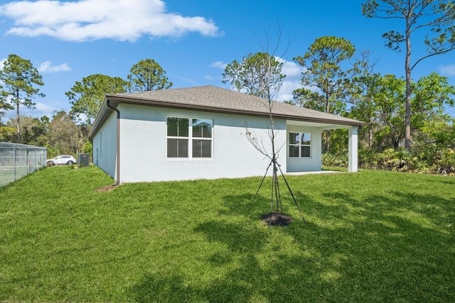 back of house featuring a shingled roof, a lawn, fence, and stucco siding