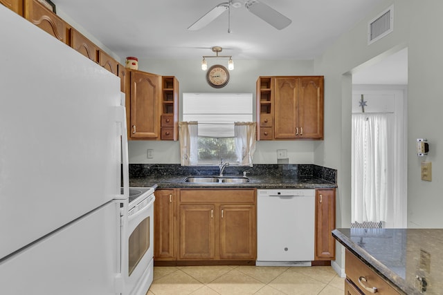 kitchen featuring sink, white appliances, light tile patterned floors, and dark stone counters