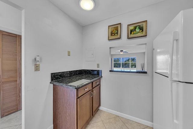 kitchen with dark stone countertops, white fridge, light tile patterned floors, and ceiling fan