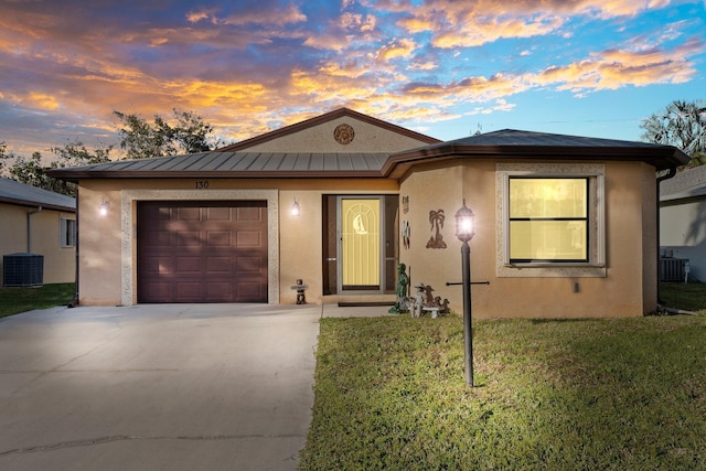 view of front of home with a garage, central AC unit, and a lawn