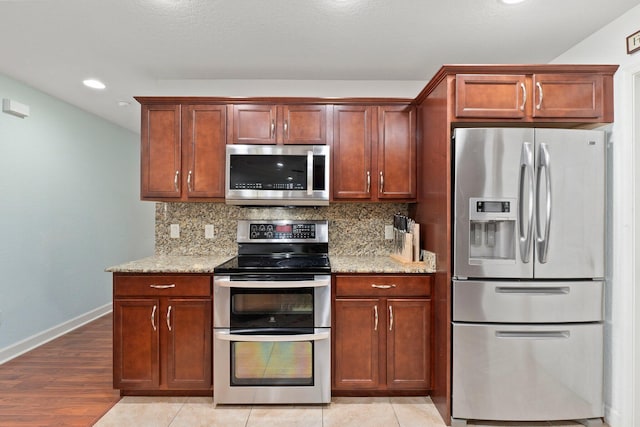 kitchen with light stone counters, stainless steel appliances, tasteful backsplash, and light hardwood / wood-style flooring