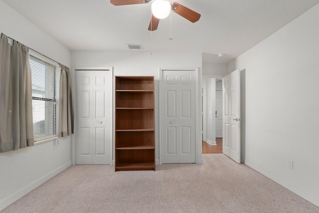 unfurnished bedroom with light carpet, ceiling fan, and multiple closets