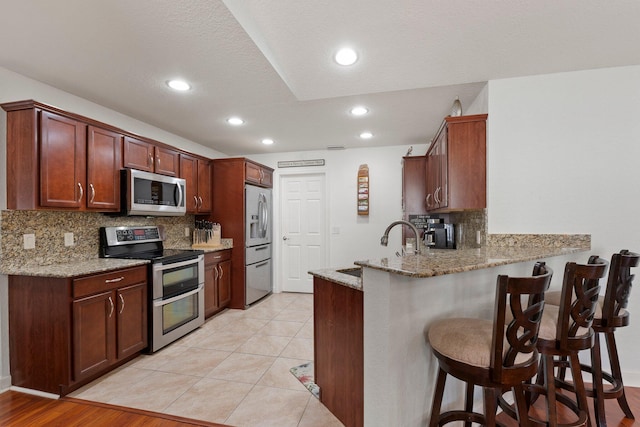 kitchen with appliances with stainless steel finishes, a kitchen breakfast bar, kitchen peninsula, light stone countertops, and backsplash