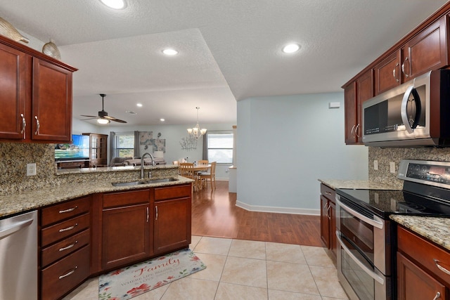 kitchen featuring appliances with stainless steel finishes, decorative light fixtures, sink, kitchen peninsula, and light stone countertops