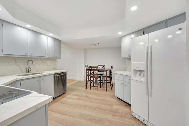 kitchen with sink, stainless steel dishwasher, white refrigerator with ice dispenser, light hardwood / wood-style floors, and decorative backsplash