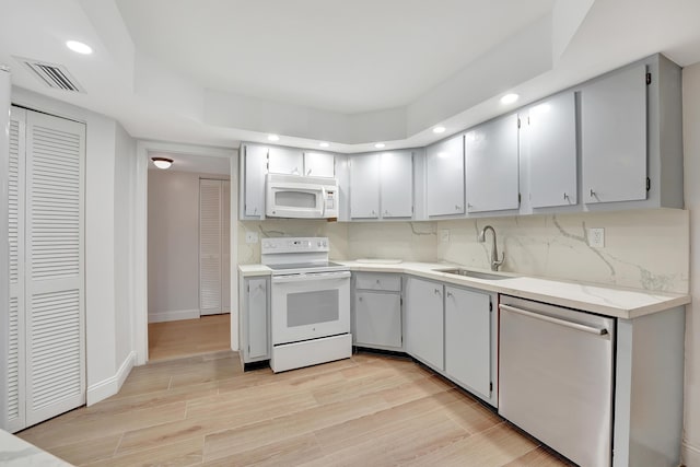 kitchen featuring gray cabinets, sink, decorative backsplash, white appliances, and light wood-type flooring