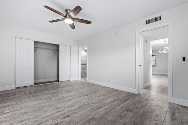 unfurnished bedroom featuring ceiling fan with notable chandelier, light hardwood / wood-style floors, and a closet