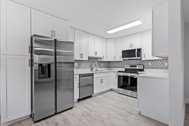 kitchen with sink, white cabinets, decorative backsplash, stainless steel appliances, and light hardwood / wood-style flooring