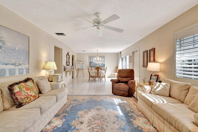 tiled living room with ceiling fan with notable chandelier and a textured ceiling