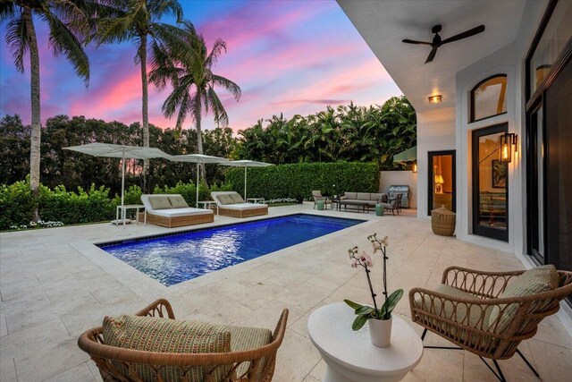 pool at dusk with ceiling fan, an outdoor hangout area, and a patio area