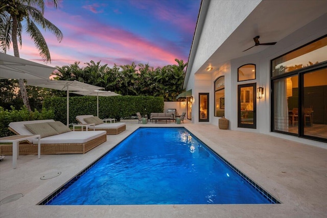 pool at dusk featuring ceiling fan, an outdoor living space, and a patio area