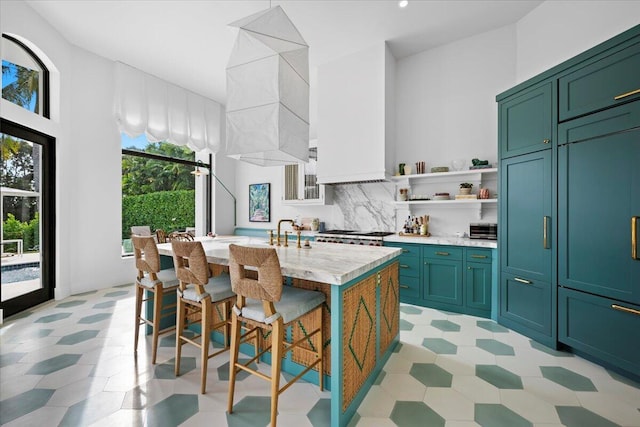 kitchen featuring a kitchen bar, sink, tasteful backsplash, a center island with sink, and light stone countertops