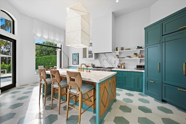 kitchen with a breakfast bar, sink, an island with sink, light stone countertops, and decorative backsplash