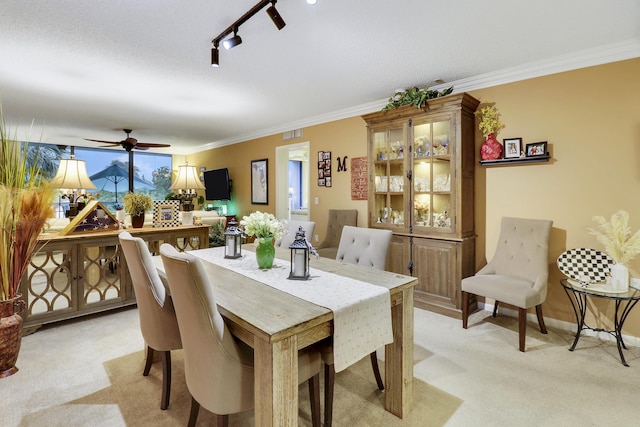 carpeted dining space featuring crown molding, track lighting, and ceiling fan