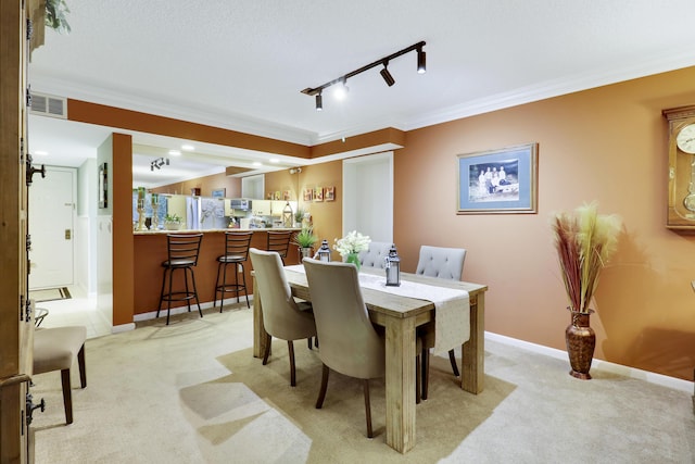 dining space with crown molding, light colored carpet, and track lighting