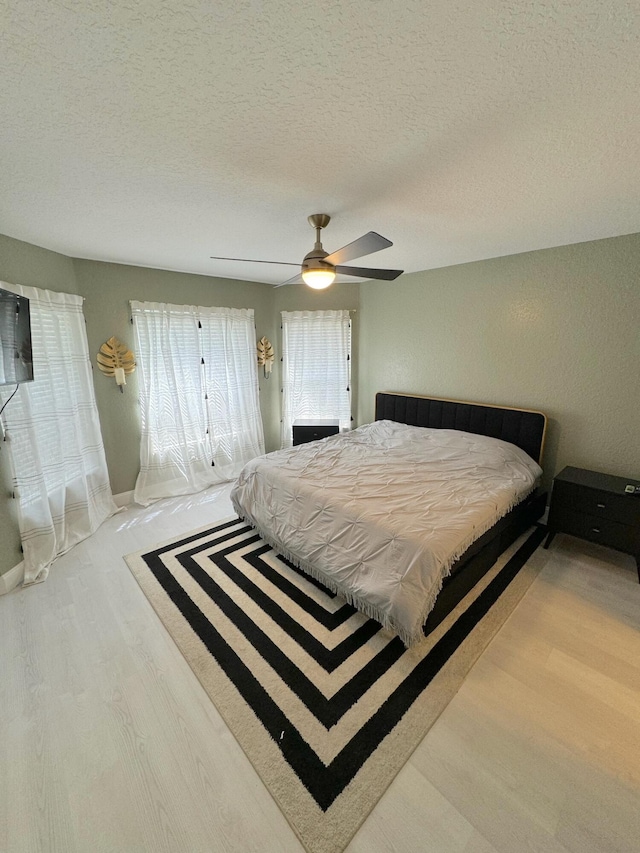 bedroom with ceiling fan, light hardwood / wood-style flooring, and a textured ceiling