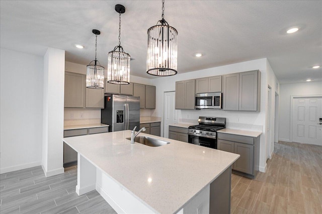 kitchen featuring appliances with stainless steel finishes, a kitchen island with sink, gray cabinets, pendant lighting, and a sink