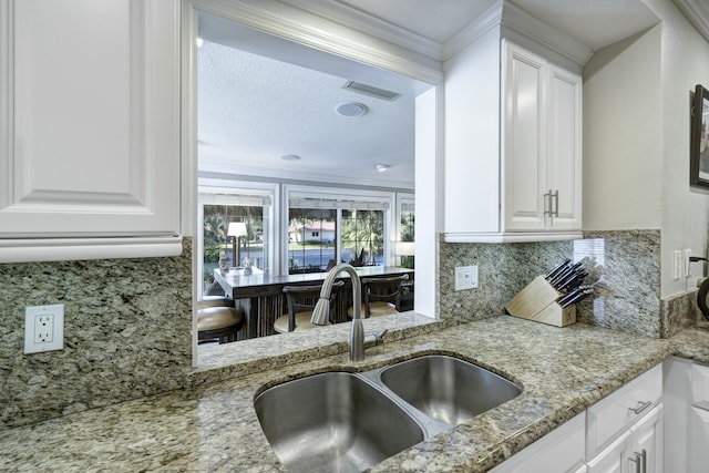 kitchen with white cabinetry, sink, light stone counters, and decorative backsplash