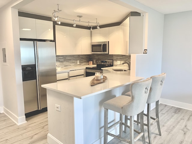 kitchen featuring white cabinets, appliances with stainless steel finishes, backsplash, and a kitchen breakfast bar