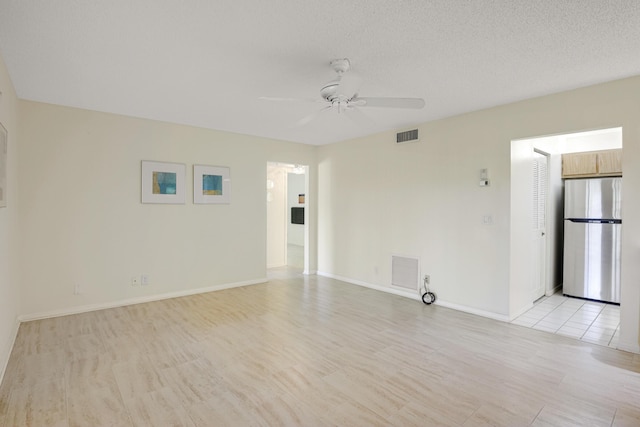 empty room with ceiling fan, a textured ceiling, and light wood-type flooring