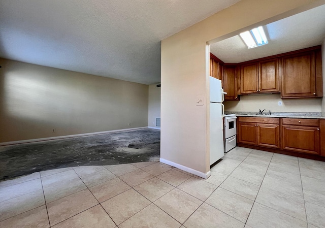 kitchen featuring sink, white appliances, light tile patterned floors, and a textured ceiling