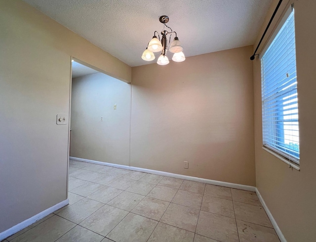 tiled spare room featuring an inviting chandelier and a textured ceiling