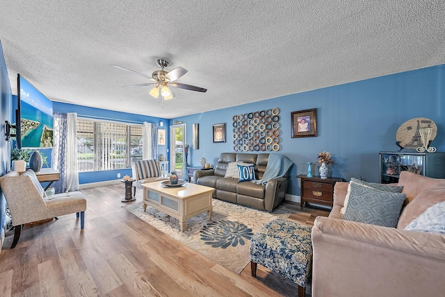 living room with ceiling fan, a textured ceiling, and light wood-type flooring