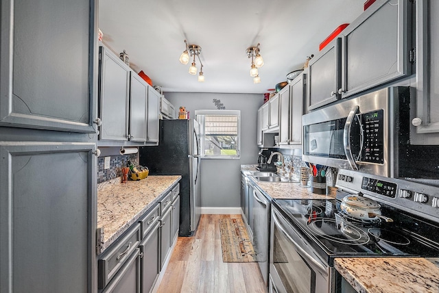 kitchen with light stone counters, sink, light wood-type flooring, and appliances with stainless steel finishes