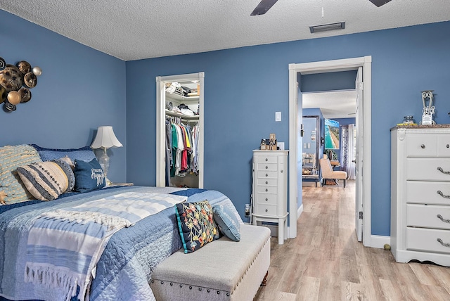 bedroom with ceiling fan, a textured ceiling, a walk in closet, a closet, and light wood-type flooring