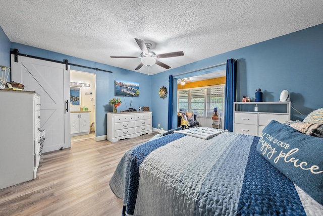 bedroom featuring ensuite bath, ceiling fan, light hardwood / wood-style floors, a textured ceiling, and a barn door