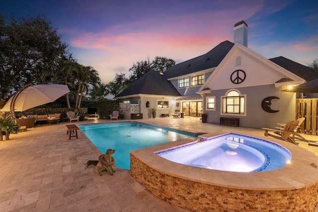 pool at dusk with an in ground hot tub and a patio area