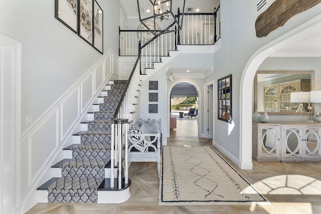 entrance foyer with light parquet flooring, a towering ceiling, a chandelier, and crown molding