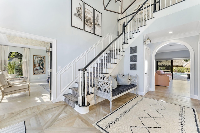 stairway with parquet floors, a towering ceiling, and ornamental molding