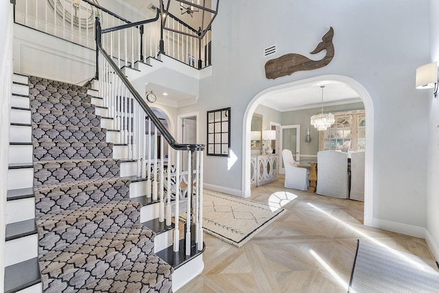 entrance foyer featuring crown molding, a towering ceiling, light parquet flooring, and a notable chandelier