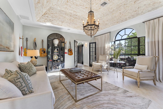 living room featuring brick ceiling, an inviting chandelier, a tray ceiling, ornamental molding, and light hardwood / wood-style floors