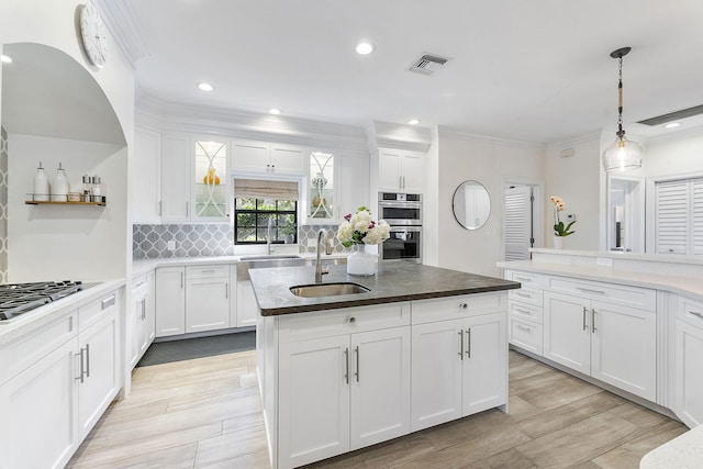 kitchen featuring an island with sink, sink, white cabinets, and decorative light fixtures