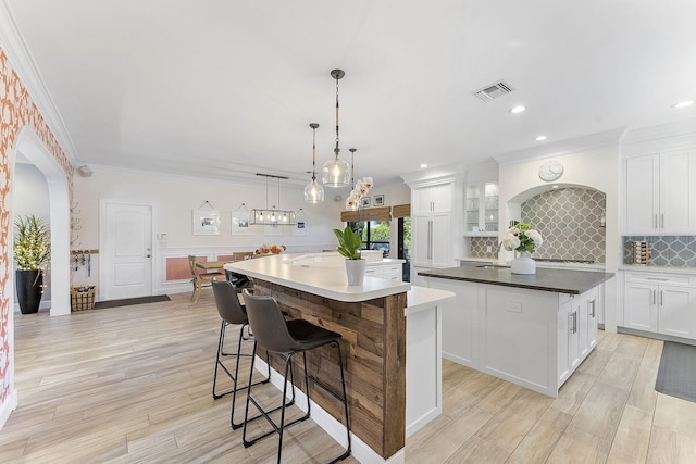 kitchen with a breakfast bar, pendant lighting, backsplash, white cabinets, and a large island