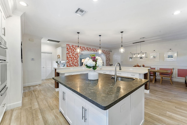 kitchen with hanging light fixtures, a kitchen island with sink, and white cabinets