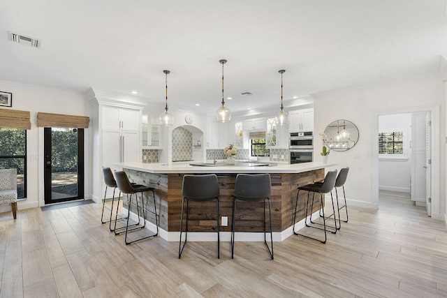 kitchen with a large island with sink, hanging light fixtures, white cabinets, and a kitchen breakfast bar