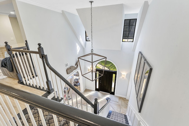 foyer entrance with crown molding, a towering ceiling, light parquet flooring, and a chandelier