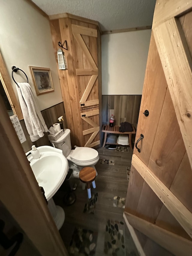 bathroom with wood-type flooring, wooden walls, sink, and a textured ceiling