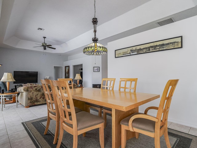 tiled dining space featuring a raised ceiling and ceiling fan