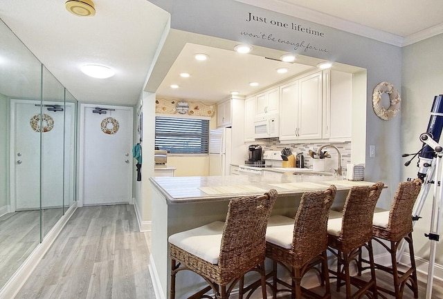 kitchen featuring sink, white cabinets, a kitchen breakfast bar, kitchen peninsula, and white appliances