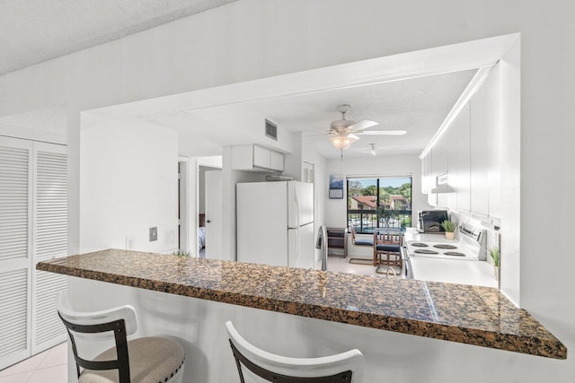 kitchen featuring range with electric cooktop, a breakfast bar, white cabinetry, white fridge, and kitchen peninsula